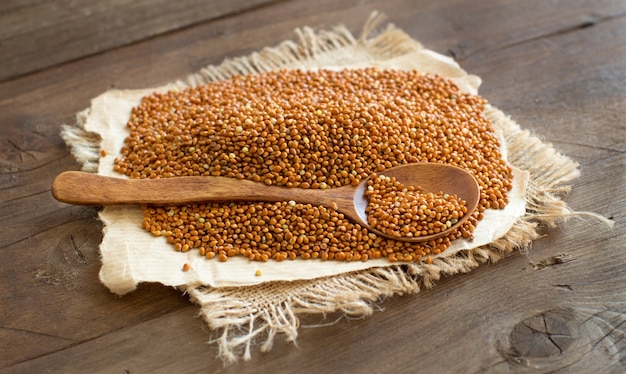 Whole brown millet pile with a spoon on wooden table close up