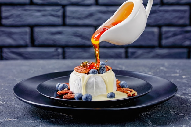 Whole Camembert cheese with pecan, blueberries served on a black plate on a concrete table, horizontal view, close-up