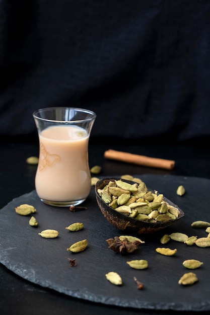 Foto cardamomo intero in piastra di guscio di cocco in primo piano a fuoco e tradizionale tè karak orientale o masala chai sullo sfondo messa a fuoco selettiva sfondo scuro cucina esotica