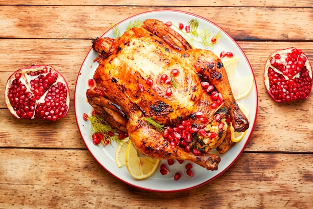 Whole chicken baked with pomegranate berries in plate on a wooden rustic old background.