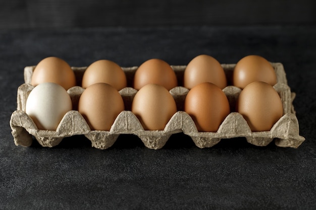 Целые куриные яйца в картонном лотке на темном фоне, выборочный фокус