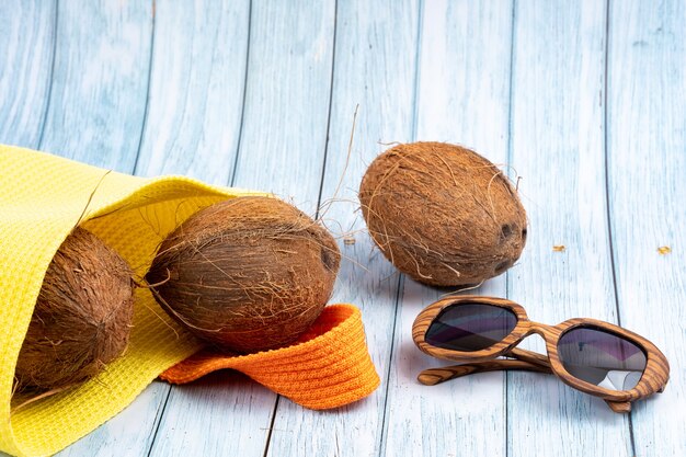 Whole coconuts lying in a yellow bag and glasses on a blue wooden background