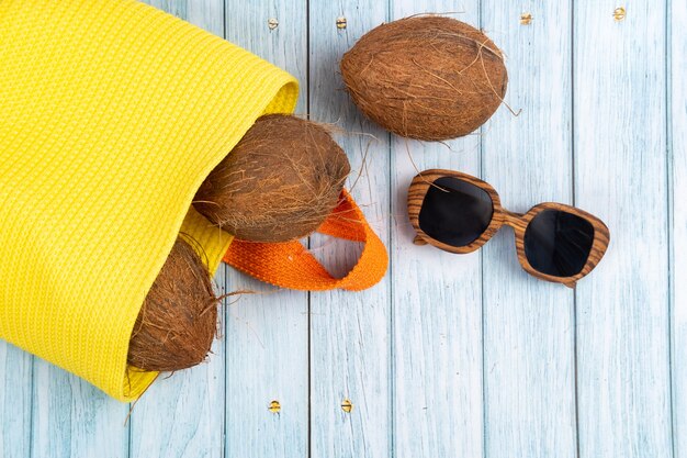Целые кокосы, лежащие в желтом мешке и очках на синем деревянном фоне.
