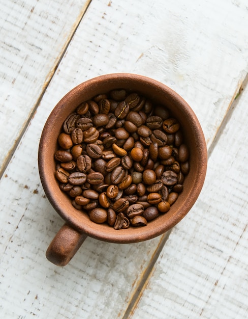 木の床に立つ茶色のカップに丸ごとコーヒー豆