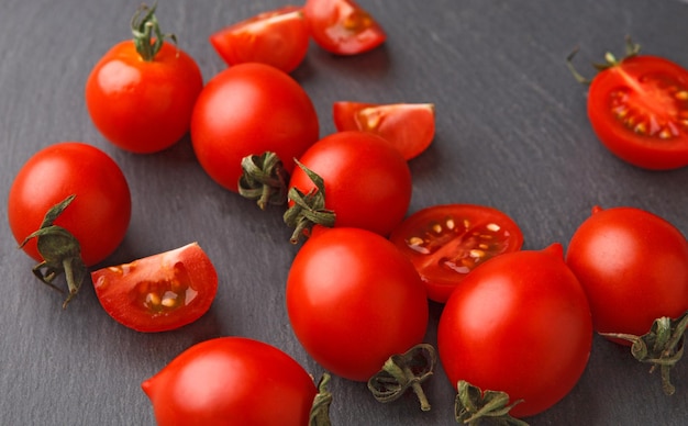 Whole and cut cherry tomatoes on rustic slate stone plate. Cooking healthy food on gray background with copy space. Fresh organic vegetables for everyday meals, closeup.