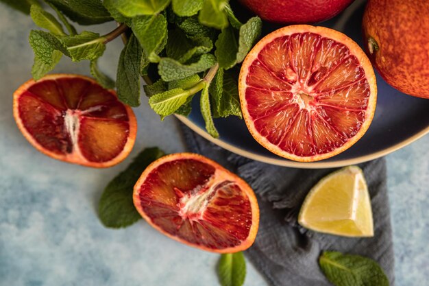 Whole and cut in half blood Sicilian oranges, limes and mint on blue concrete background. Top view.