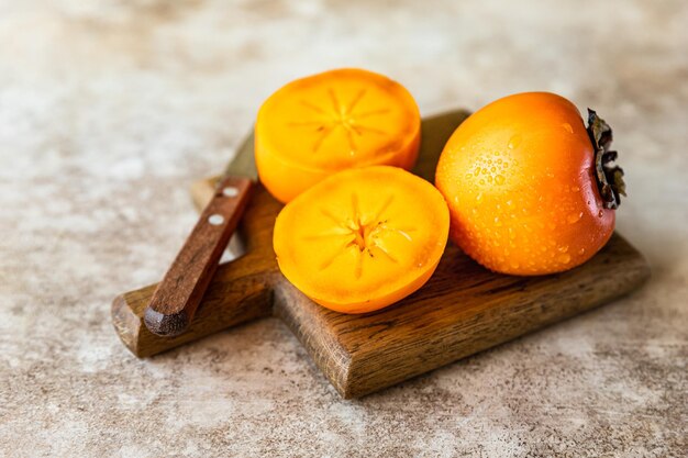 Whole and cut half ripe orange persimmon fruit on wooden cutting board, concrete background.