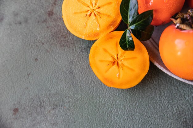 Whole and cut persimmon fruit with water drops and green leaves