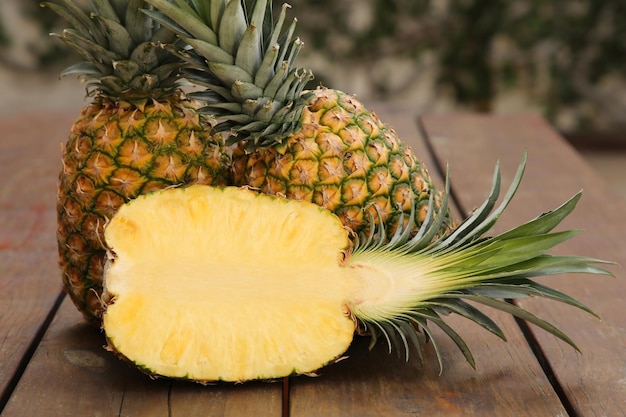 Whole and cut ripe pineapples on wooden table closeup