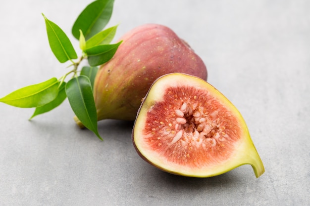 Whole figs and one fig sliced in half on top of a gray table