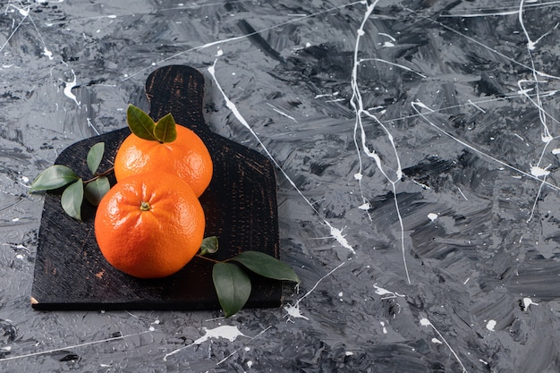 Whole fresh orange fruits with leaves placed on black cutting board