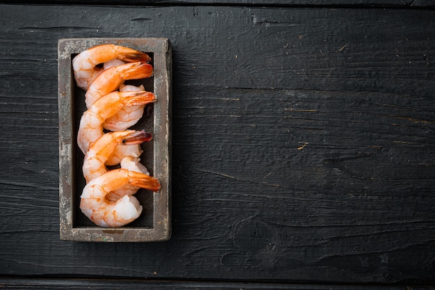 Whole fresh peeled cooked prawns, shrimps set, in wooden box, on black wooden table