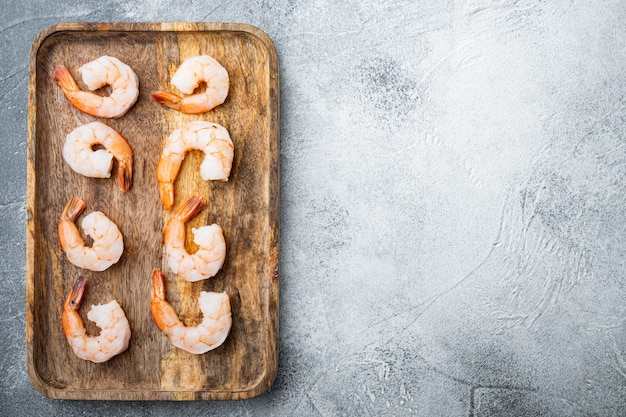 Whole fresh peeled cooked prawns, shrimps set, on wooden tray, on gray table, top view flat lay