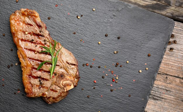 Whole fried New York beef steak on a black board,  striploin doneness rare, top view