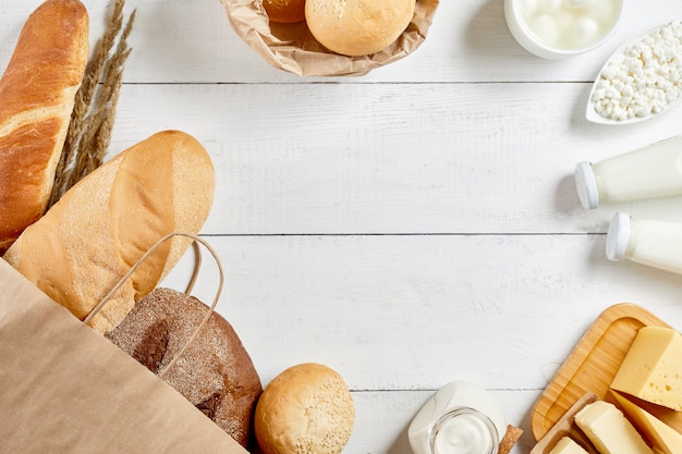 Pane integrale in sacco di carta di ecologia su fondo di legno bianco. piatti piatti alimenti biologici naturali: latte, formaggio, panna acida e prodotti da forno. salva il concetto di ecologia. riciclaggio zero rifiuti. copia spazio.