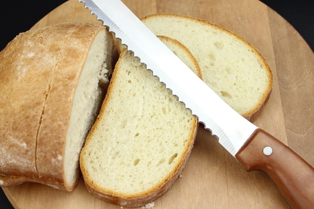 Pane integrale messo su tavola di legno da cucina con un coltello da chef per il taglio su sfondo nero