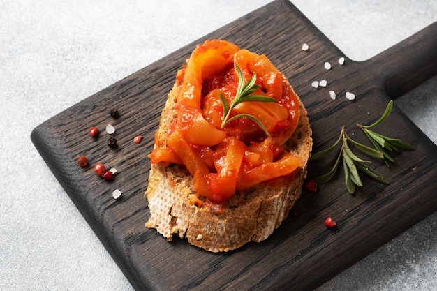 Цельнозерновой хлеб бутерброды с консервированным перцем с помидорами на деревянной разделочной доске.