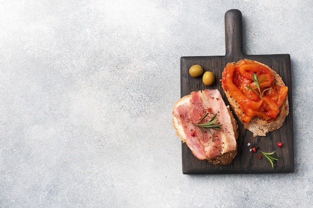 Whole grain bread sandwiches with cream cheese, bacon and canned peppers with tomato on a wooden cutting Board.