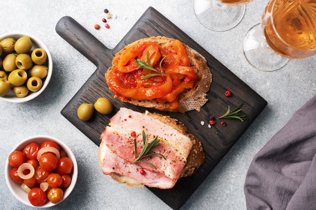 Whole grain bread sandwiches with cream cheese, bacon and canned peppers with tomato on a wooden cutting Board.