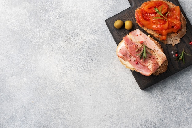 Whole grain bread sandwiches with cream cheese, bacon and canned peppers with tomato on a wooden cutting Board.