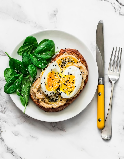 Whole grain grilled bread hummus boiled egg sesame sandwich and fresh spinach on a light background top view