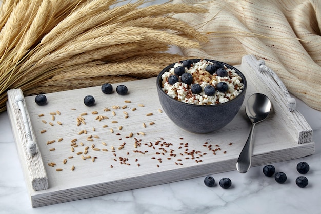 Whole grain oatmeal with blueberries, flax seeds and cottage cheese on a white painted tray surrounded by ears of corn and a tea towel