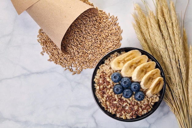 Whole grain oatmeal with flax seeds with blueberries and banana slices and paper cuns with scattered oats grains on a white marble table. Energy and health food. Top view with copy space. Flat lay.