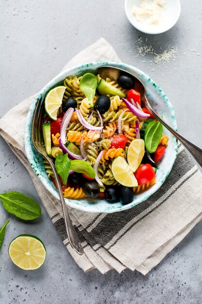 Whole grain pasta with vegetables on a white plate on a light grey slate, stone or concrete background. Top view with copy space.