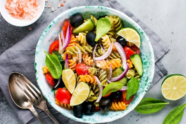 Whole grain pasta with vegetables on a white plate on a light grey slate, stone or concrete background. Top view with copy space.