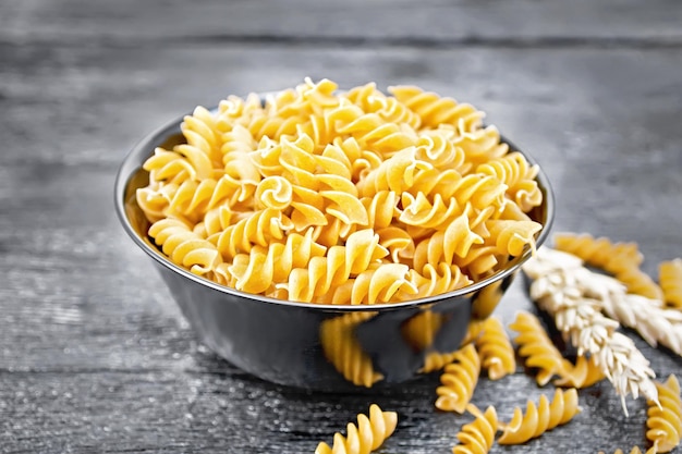 Whole grain wheat flour fusilli pasta in a bowl spikelets of wheat on a dark wooden board background