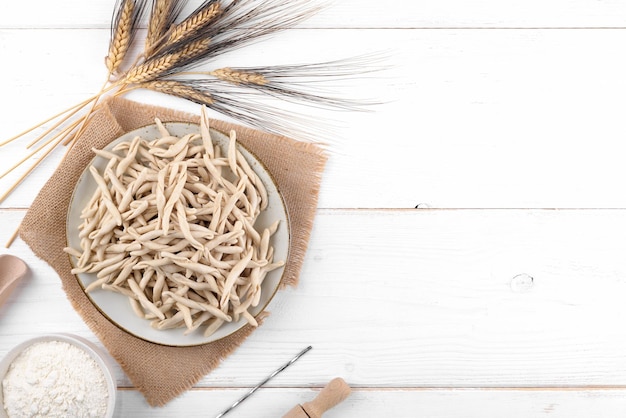 Photo whole grain wheat raw apulian pasta called pizzarieddi or maccaruni on a ceramic plate on white wooden table