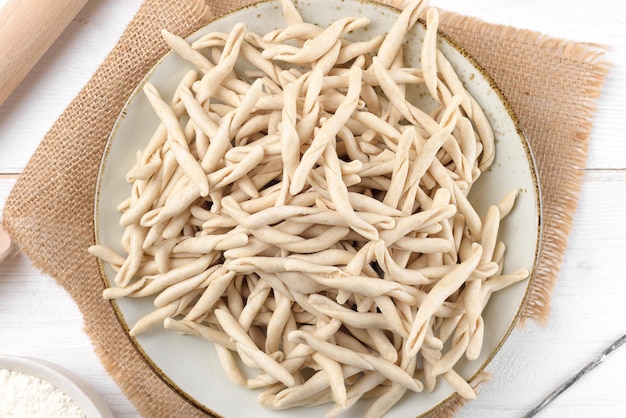 Photo whole grain wheat raw apulian pasta called pizzarieddi or maccaruni on a ceramic plate on white wooden table