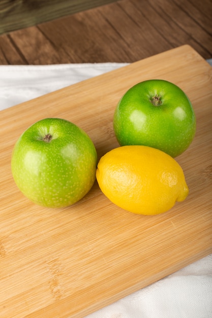 Whole green apples and a lemon on a wood board