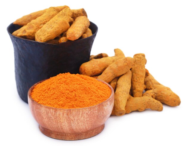 Whole and ground turmeric with mortar and pestle over white background