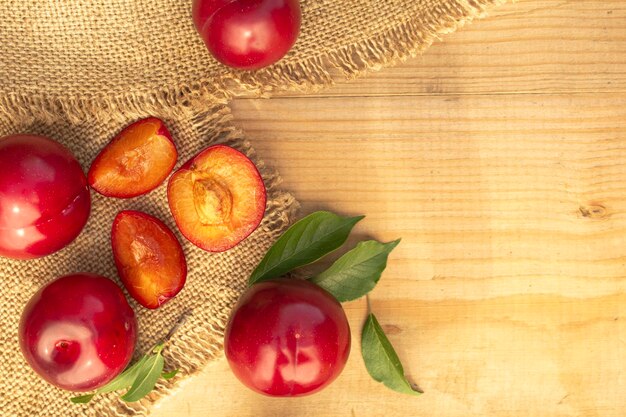 Whole and halved red plums lie on a wooden table