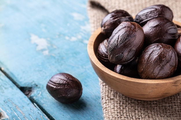 Whole inshell nutmeg nuts in a bowl on blue rustic wooden table.