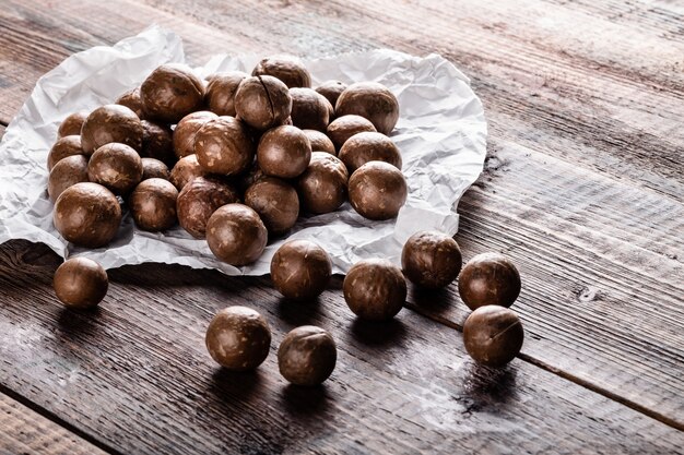 Whole Macadamia nuts on white paper on old wooden rustic table 