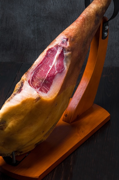 Whole mediterranean traditional jamon on a wooden stand with a knife lean on a table dark image