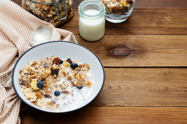 Фото Цельнозерновой завтрак, мюсли с сухофруктами и черникой, молоко и мед.