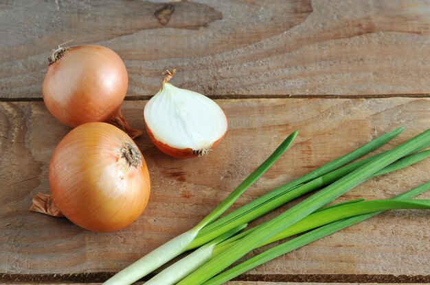 Whole onions, chopped and green onion on a rough wooden background