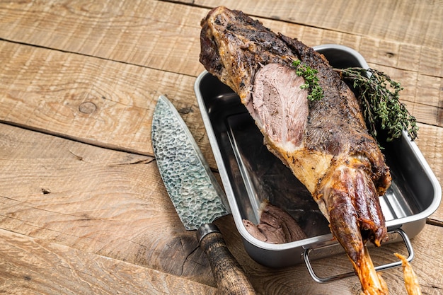 Whole oven roasted goat leg meat with thyme in a steel tray Wooden background Top view Copy space