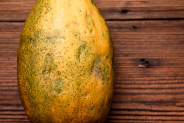 Whole papaya on a wooden background An imperfectlooking fruit with an uneven surface