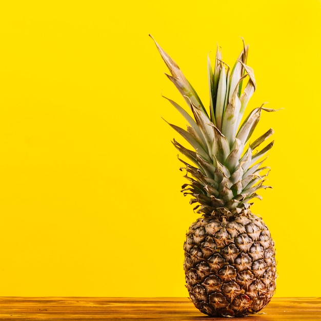 Whole pineapple on table against yellow background