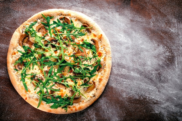 Foto una pizza intera con rucola, formaggio, funghi porcini e olio al tartufo. ricetta pizza italiana su fondo di legno marrone. vista dall'alto e copia spazio