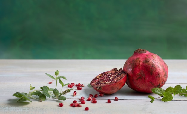 Whole pomegranate next to another open on a chalk table and\
green background.