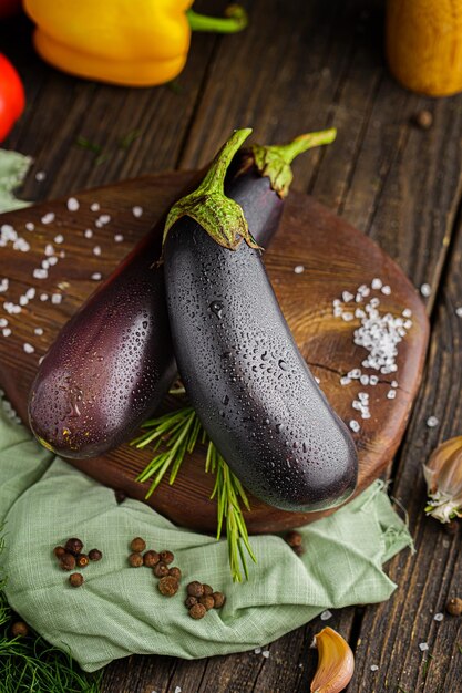 whole purple eggplant, spices and coarse salt, rustic style, cherry tomato branch, black background