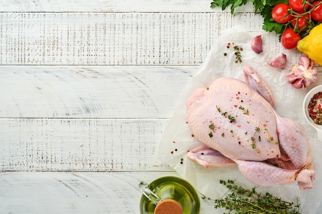 Whole raw chicken with ingredients for making rose pepper, lemon, thyme, garlic, cherry tomato, sorrel and salt in the kitchen on light grey slate, stone or concrete background. Top view