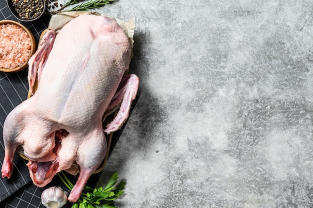 Whole raw goose. Recipe for cooking with pink salt, garlic, parsley and rosemary background