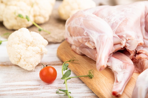 Whole raw rabbit with cauliflower, tomatoes and spices on a white wooden background and linen textile. Side view, close up, selective focus.