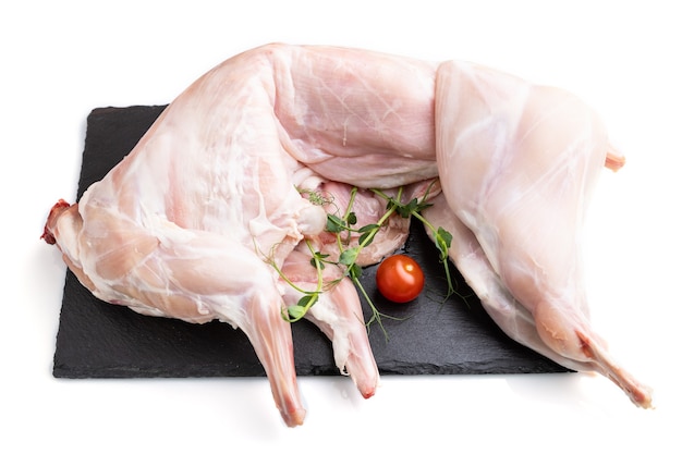 Whole raw rabbit with tomatoes, pea sprouts on a black concrete slate board